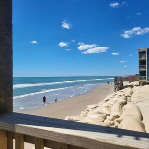 Ein Strand mit einer Holzpromenade und einem Gebäude mit mehreren Balkonen mit Blick auf den Ozean.