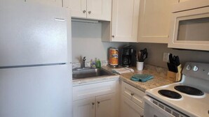 A compact kitchen with white cabinets, a refrigerator, a microwave, and a stove. - Shore To Please, 1st Floor Oceanfront Condo (North Topsail Beach)