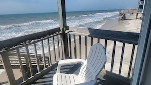A covered outdoor area with a white plastic chair, a wooden deck, and a view of the ocean. - Shore To Please, 1st Floor Oceanfront Condo (North Topsail Beach)