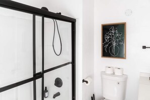 A modern bathroom with a glass shower enclosure, a toilet, and a framed abstract art piece on the wall.