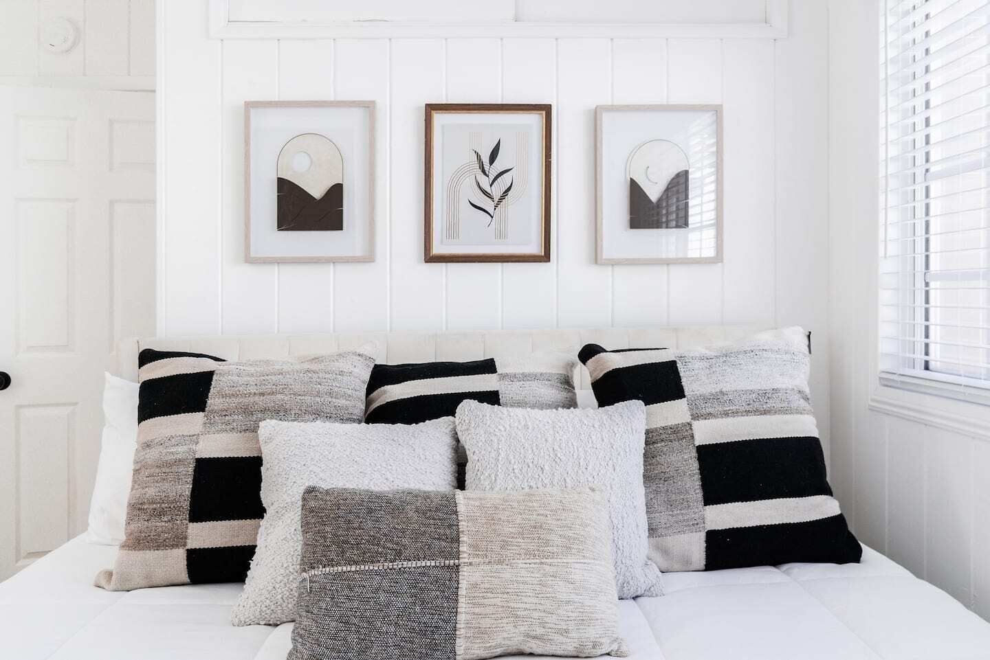 A bed with multiple pillows and three framed artworks on the wall.