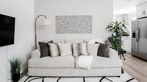 A modern living room with a sofa, a wall-mounted TV, a floor lamp, and a large abstract painting.