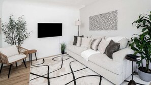 A modern living room with a sofa, a television, a patterned rug, and a potted plant.