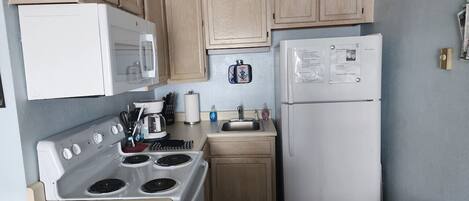 A kitchen with wooden cabinets, a white stove, a microwave, a sink, and a refrigerator.