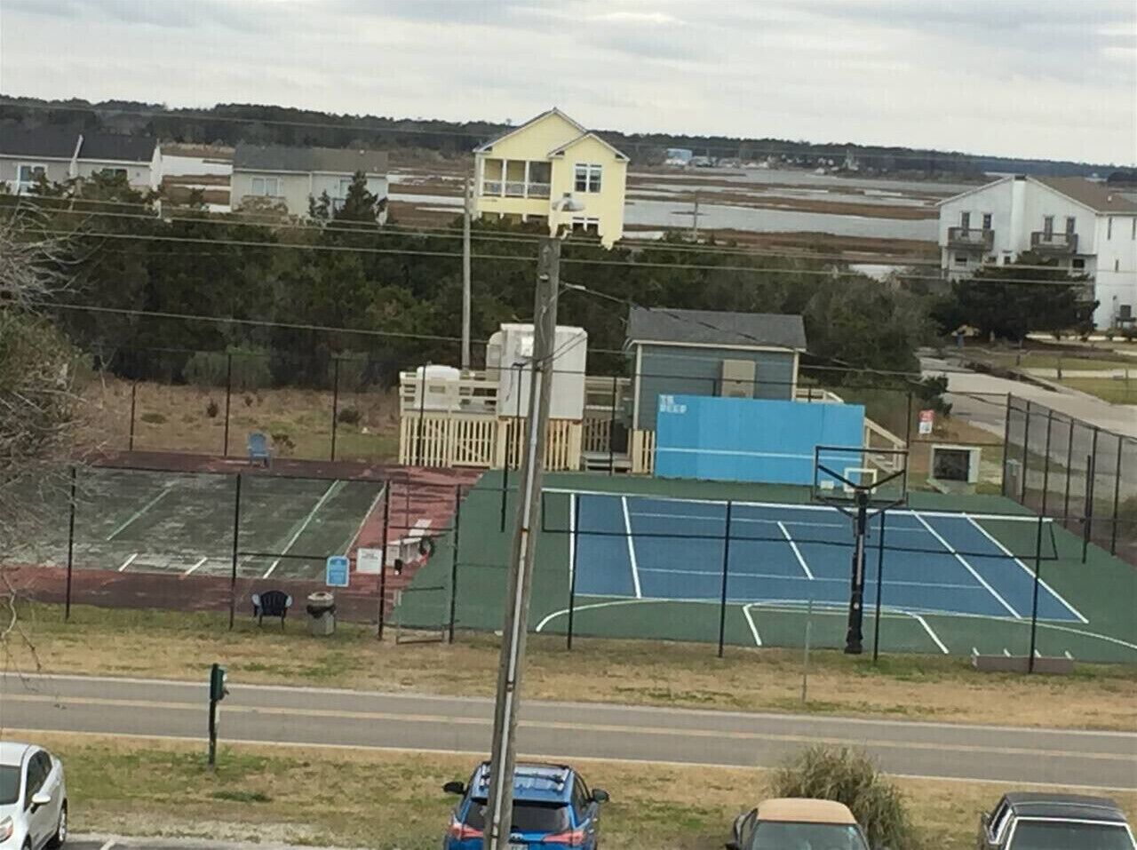 Ein Tennisplatz mit direkt angrenzendem Basketballplatz, umgeben von einem Zaun.