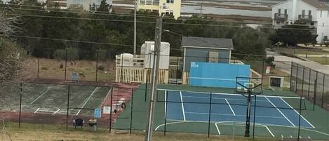 Ein Tennisplatz mit direkt angrenzendem Basketballplatz, umgeben von einem Zaun.