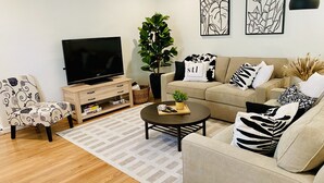 Un salon moderne avec un téléviseur à écran plat, un canapé beige, un fauteuil à motifs et une table basse.