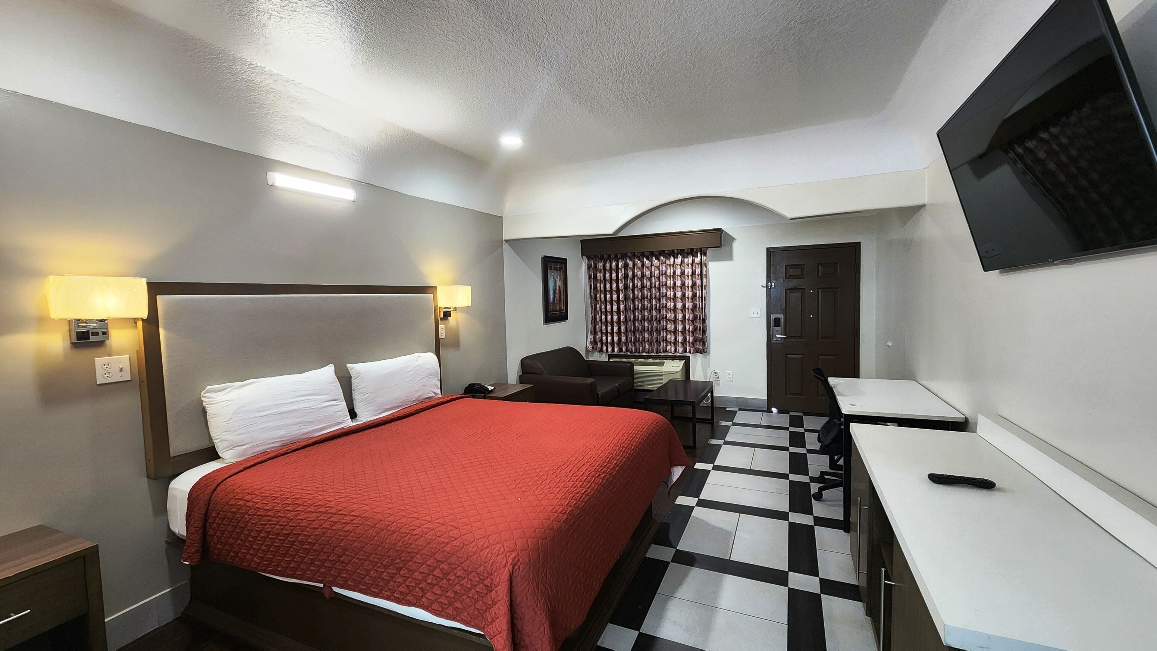 Ein Hotelzimmer mit Bett, Schreibtisch, Sessel, Fernseher und einer Rezeption.