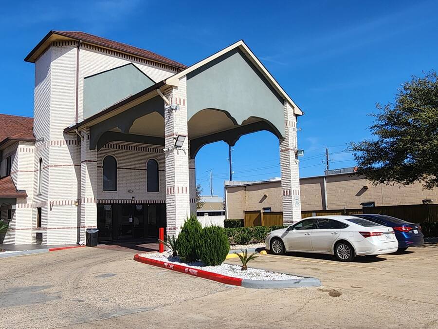A building with a large arched entrance, a parking lot, and a tree.