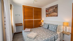 Een slaapkamer met een bed, nachtkastjes, een houten garderobe, een douchegedeelte en een kunstwerk aan de muur.