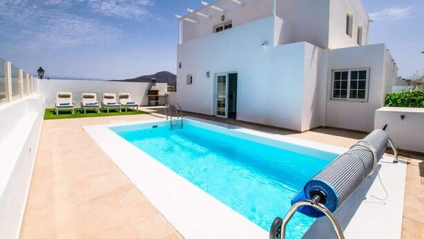 A modern building with a swimming pool, a covered outdoor area, and a view of the sea. - Casa Luca - Modern Escape by Villas Now (Playa Blanca)