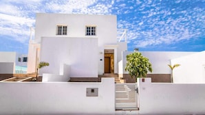 A white building with a red ground floor, a staircase, and a small garden area. - Casa Luca - Modern Escape by Villas Now (Playa Blanca)