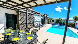 A covered outdoor dining area with a pool, stone walls, and a clear sky. - Villa Lanson - Poolside Retreat by Villas Now (Playa Blanca)