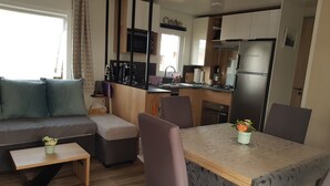 Una cocina compacta equipada con refrigerador, estufa, microondas y lavaplatos. Cuenta con una mesa de comedor con sillas y un sofá con cojines.
