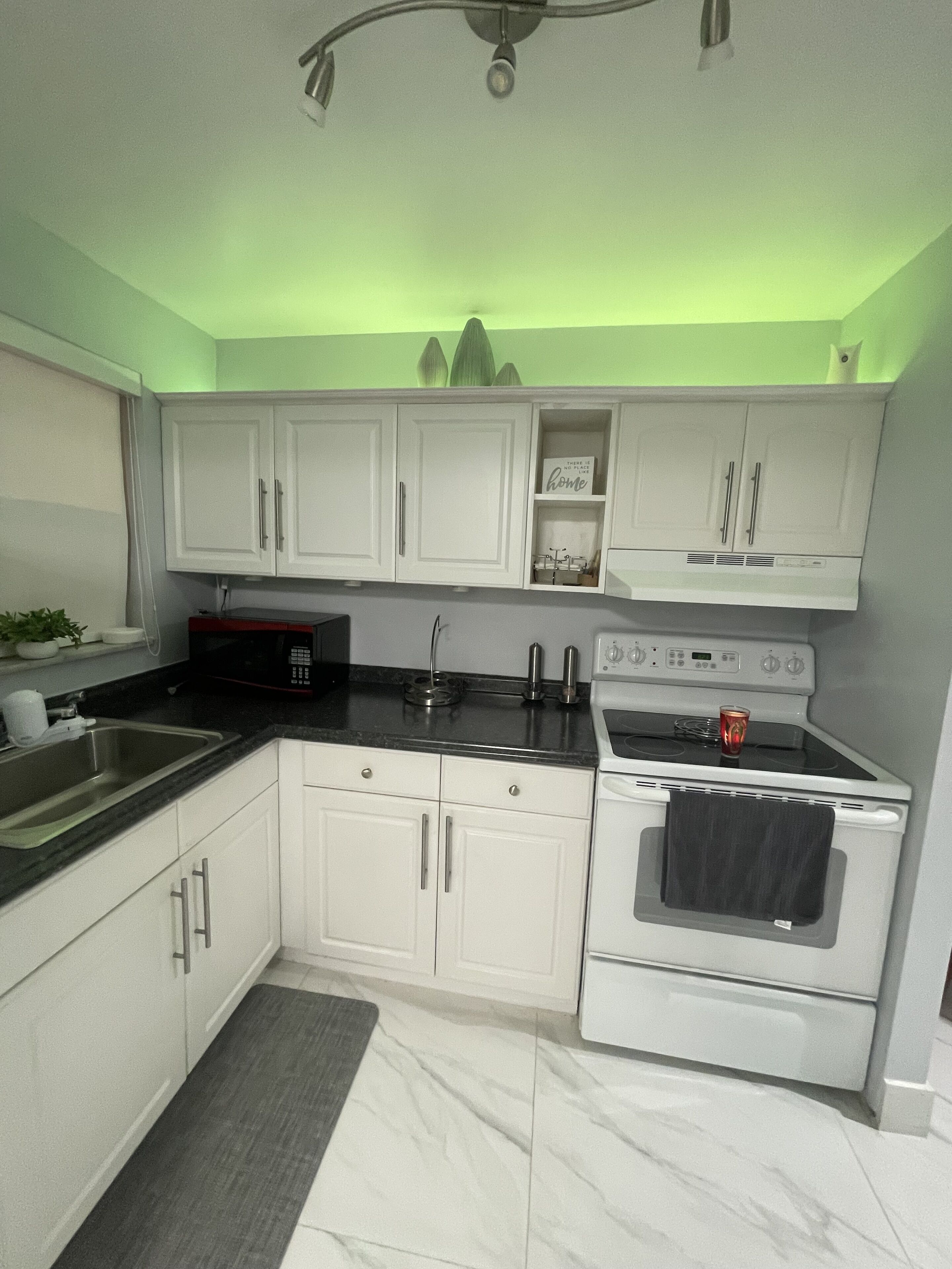 A modern kitchen with white cabinets, a black countertop, a stainless steel sink, and a white stove.