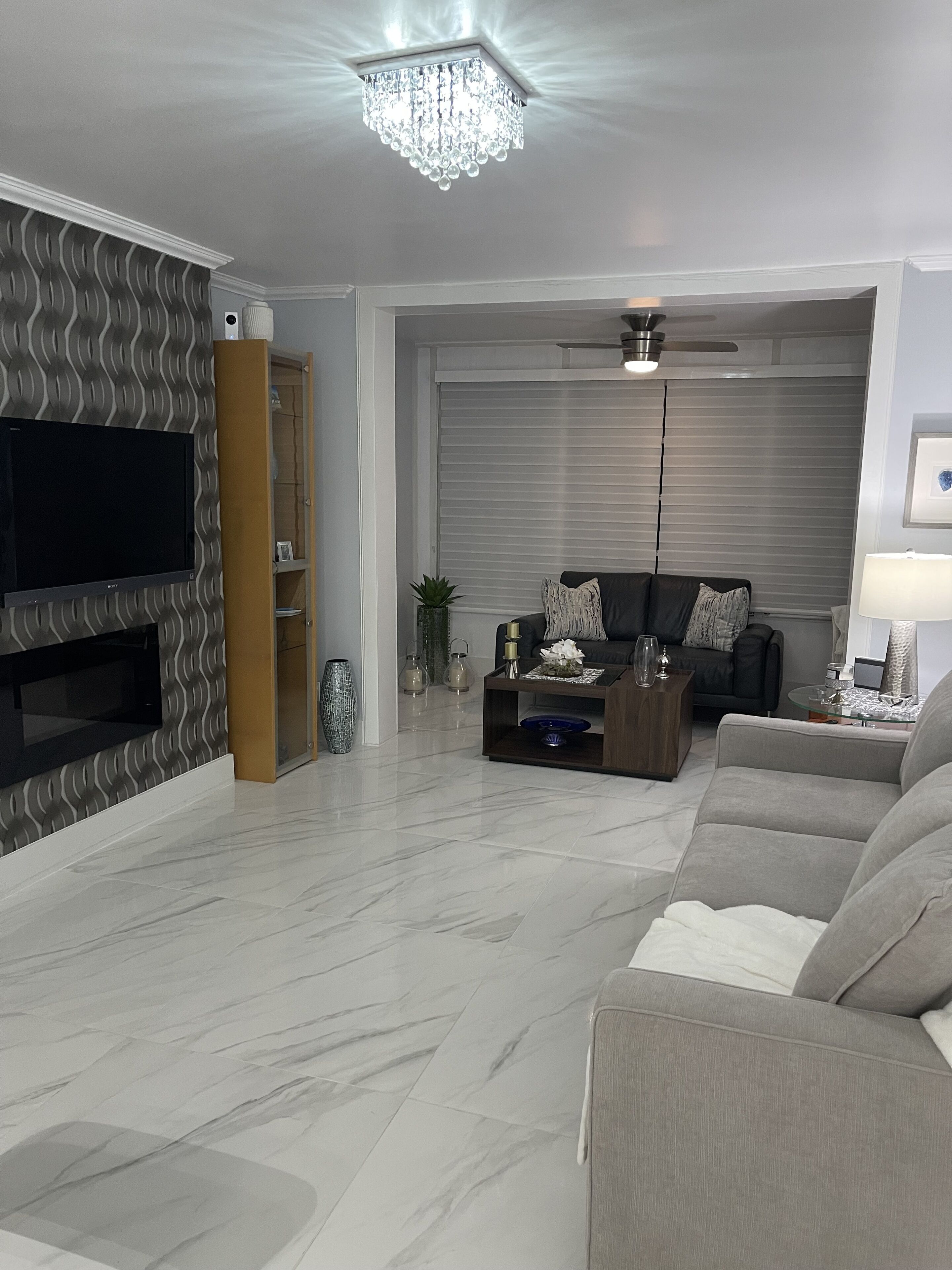 Uma sala de estar moderna com uma TV de tela plana, um ventilador de teto e uma janela grande com persianas.