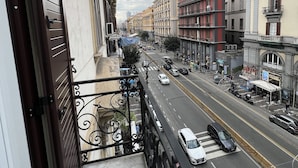 Un balcón con barandilla metálica que da a una calle urbana con edificios y coches estacionados.