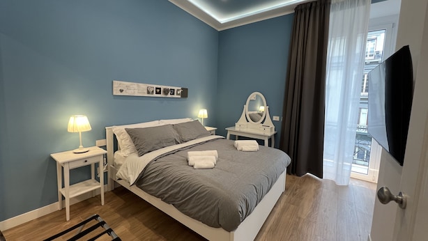 Un dormitorio moderno con cama, mesitas de noche, un espejo y un televisor.