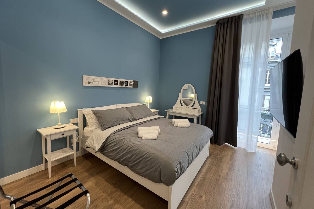 A modern bedroom with a bed, bedside tables, a mirror, and a TV.