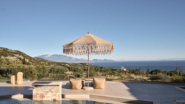 A pool with a view of the sea and mountains, a woven umbrella, and two beige cushions. - Ocean Luxury Villas (Zakynthos)