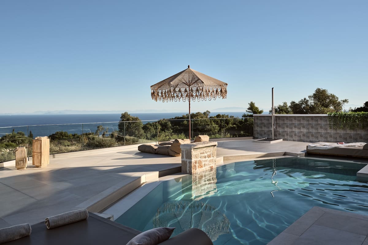 A pool area with a view of the sea, a pergola, and a stone wall.