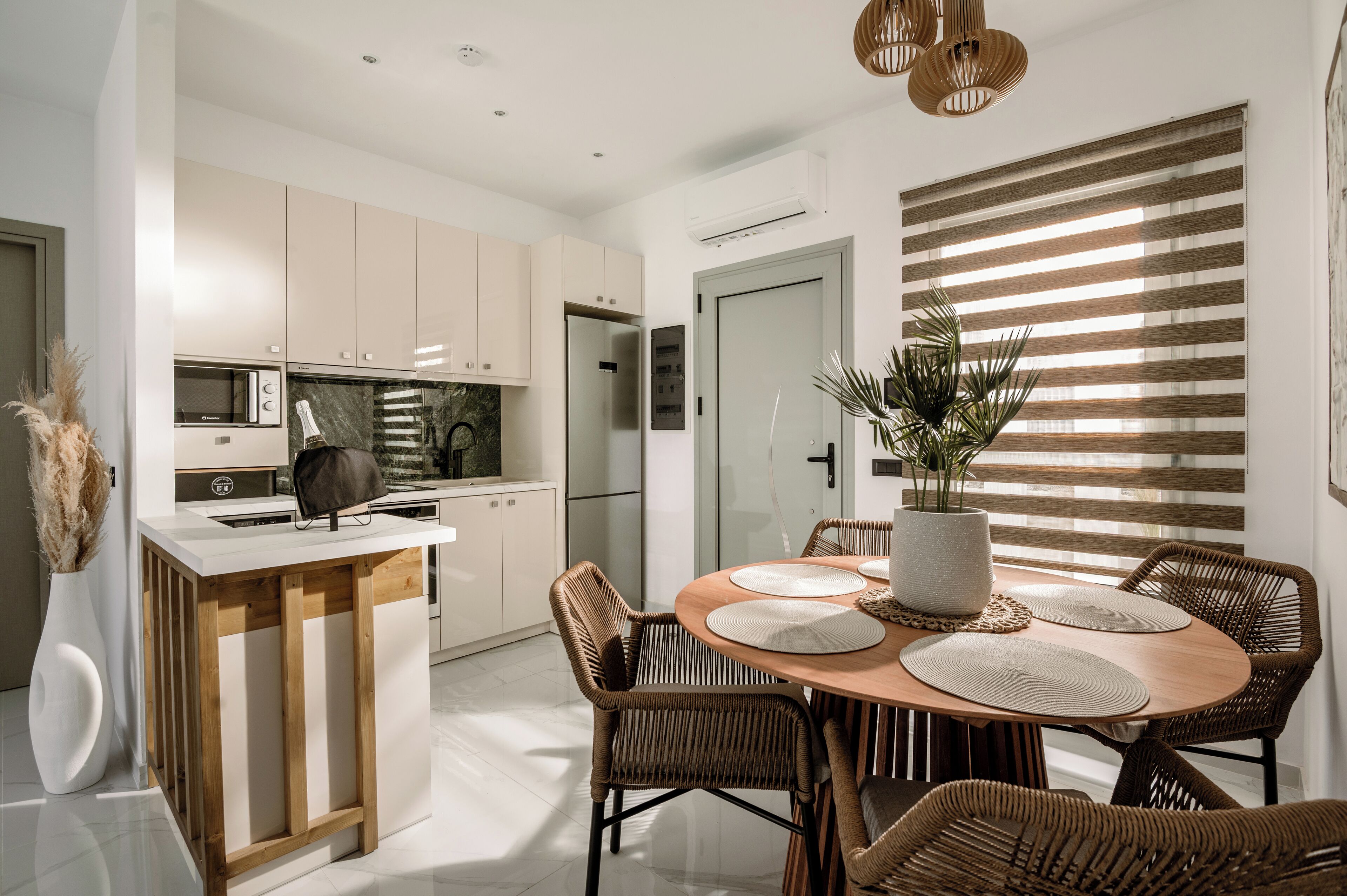 A modern kitchen with white cabinets, a central island, and a dining area with wicker chairs and a wooden table.