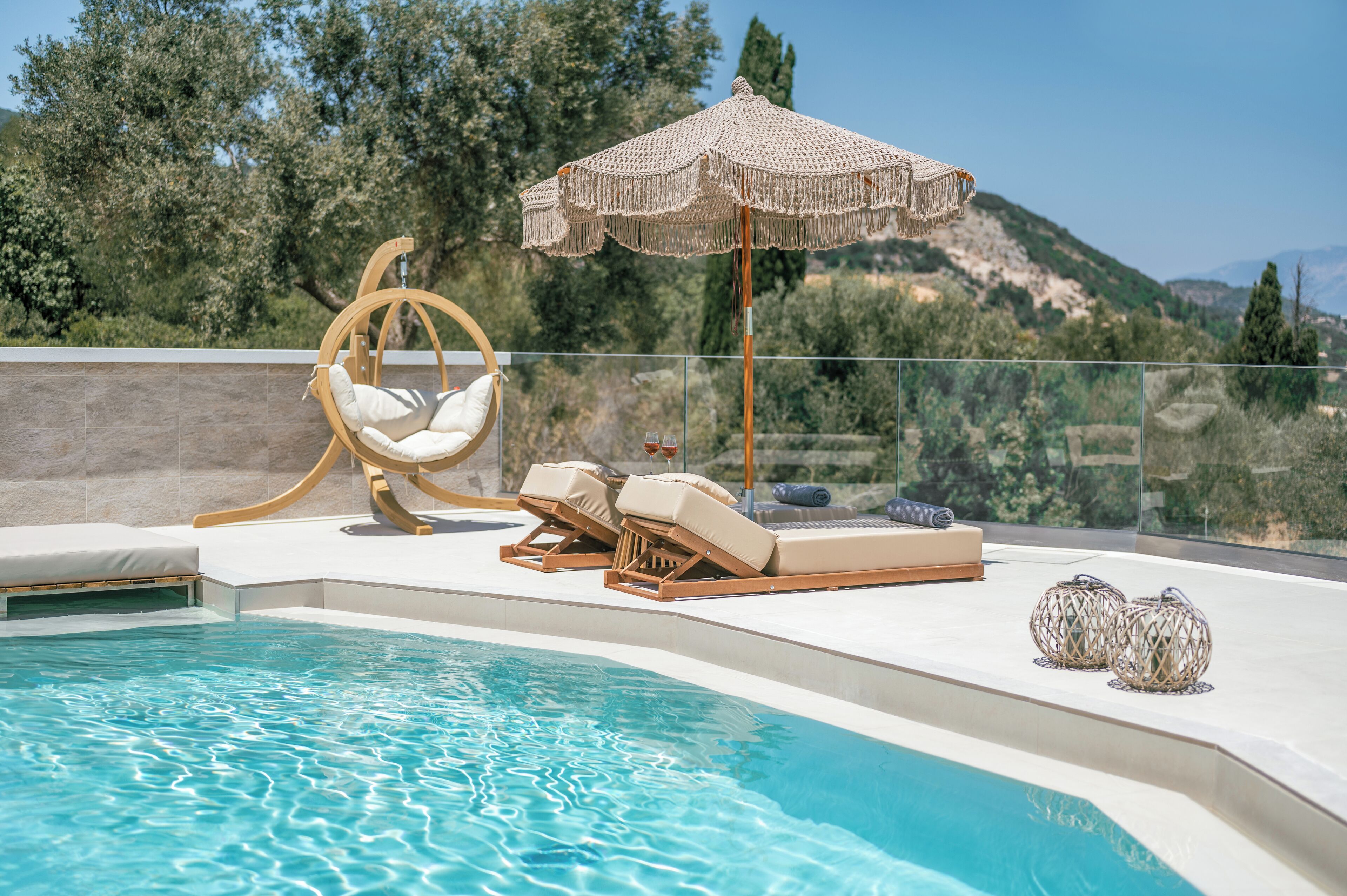 Zona junto a la piscina con una silla colgante, sillones de descanso, un parasol tejido y faroles decorativos.