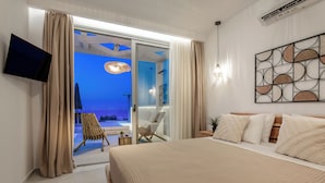 A modern bedroom with a large bed, a flat-screen TV, a ceiling fan, and a view of the beach through the sliding glass door. - Ocean Luxury Villas (Zakynthos)