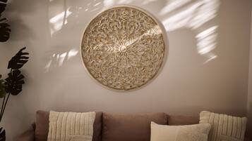 Un canapé marron avec trois coussins beige, un élément décoratif rond fixé au mur et une grande plante sur la gauche.