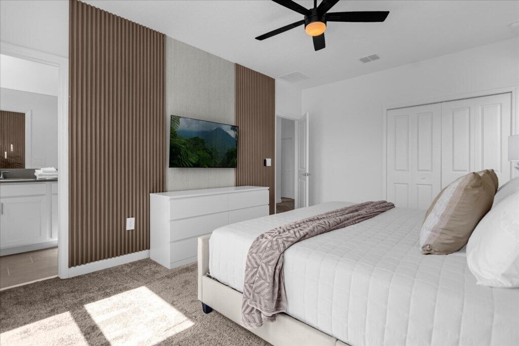 Une chambre à coucher avec un lit, un ventilateur de plafond, une télévision et une armoire.