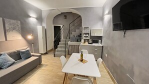 A modern living space with a dining area, a sofa, a TV mounted on the wall, and a staircase leading to an upper level. - Appartamento nel Cuore di Napoli (Nápoles)