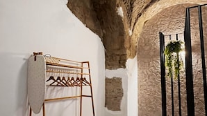 A room with exposed stone walls, a wooden hanger rack, a hanging light fixture, and a black metal structure with plants. - Appartamento nel Cuore di Napoli (Nápoles)