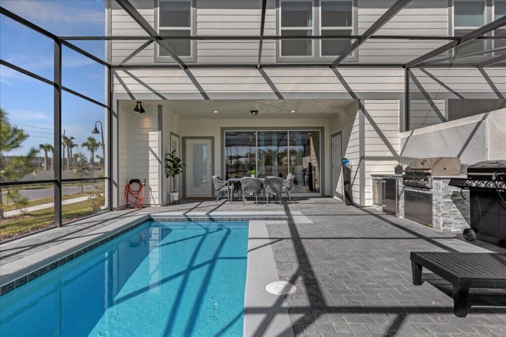 A modern pool area with a glass-enclosed patio, outdoor seating, and a barbecue grill.