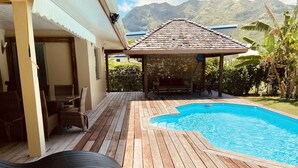 A wooden deck with a swimming pool, outdoor furniture, and a covered seating area.