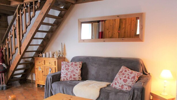 Een gezellige woonkamer met een grijze bank, decoratieve kussens, een houten salontafel, een houten kast en een houten trap.