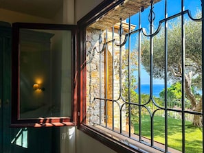 Quarto com janela que dá para uma parede de pedra e vista para o mar.