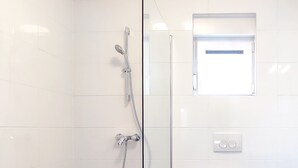 A bathroom with a glass partition, a shower, a toilet, and two green rugs on the floor.