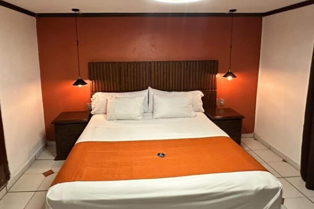 Une chambre d’hôtel comprenant un lit, deux tables de chevet, une tête de lit et deux lampes suspendues.