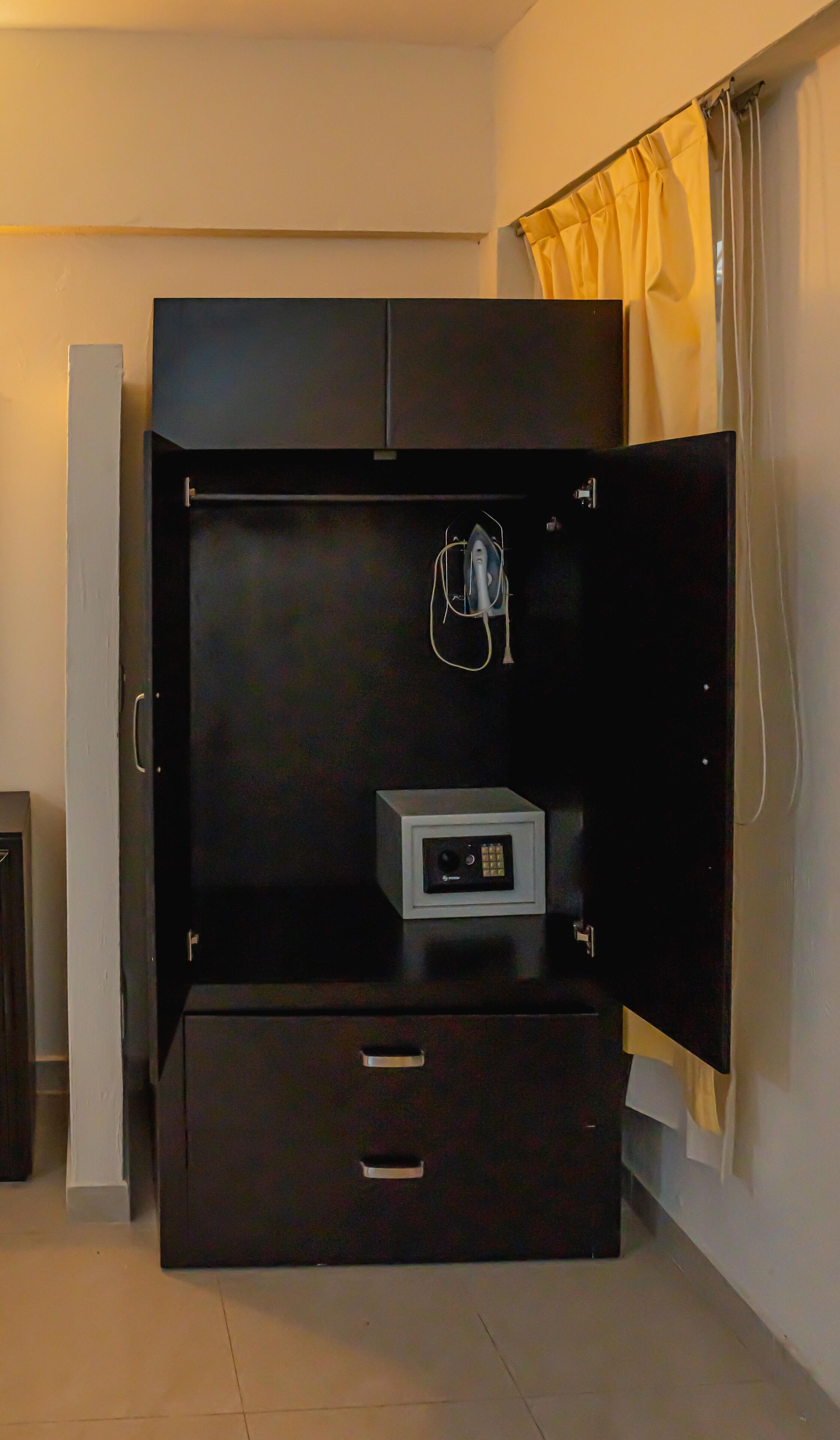 A room with a large black wardrobe, a small white cabinet, and a curtain.