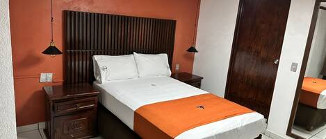 Une chambre d’hôtel avec un lit, des tables de chevet, une tête de lit en bois, un grand miroir et un ventilateur de plafond.