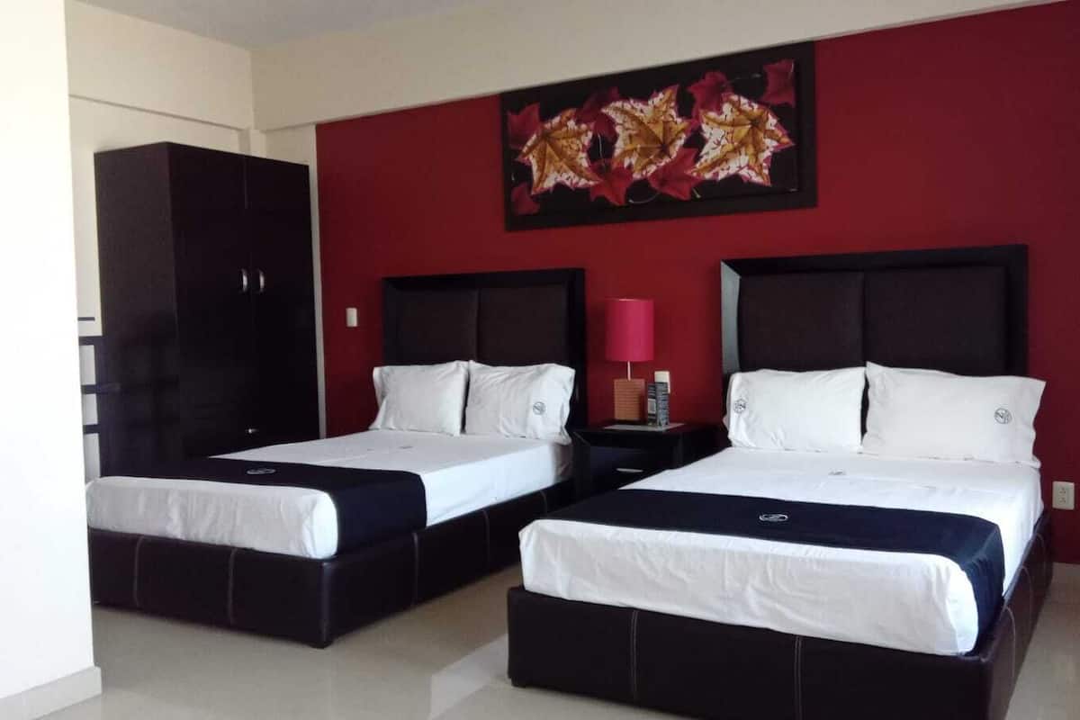 Une chambre d’hôtel avec deux lits, un mur d’accent rouge et une œuvre d’art décorative représentant des feuilles.