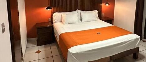 Habitación de hotel con una cama de madera, ropa de cama blanca, una mesita de noche y una lámpara moderna.