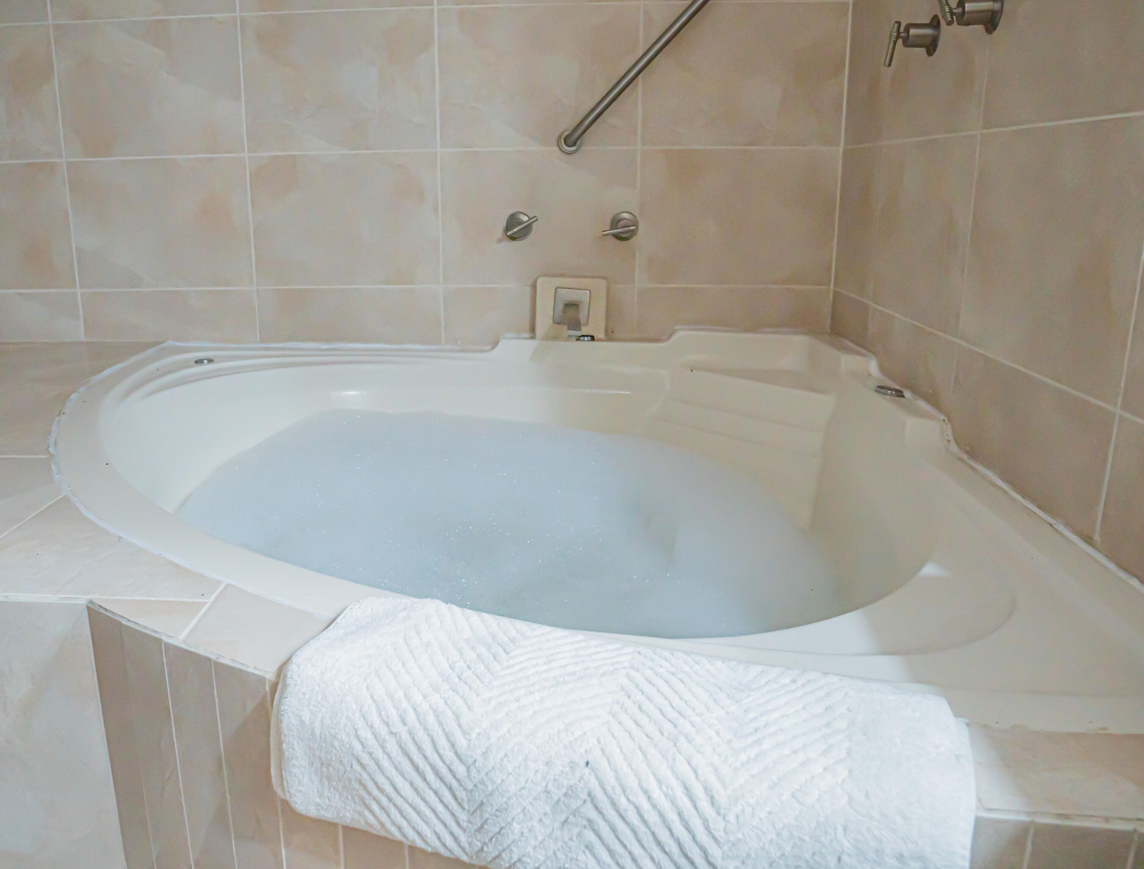 A bathtub with a white towel, a grab bar, and a control panel.