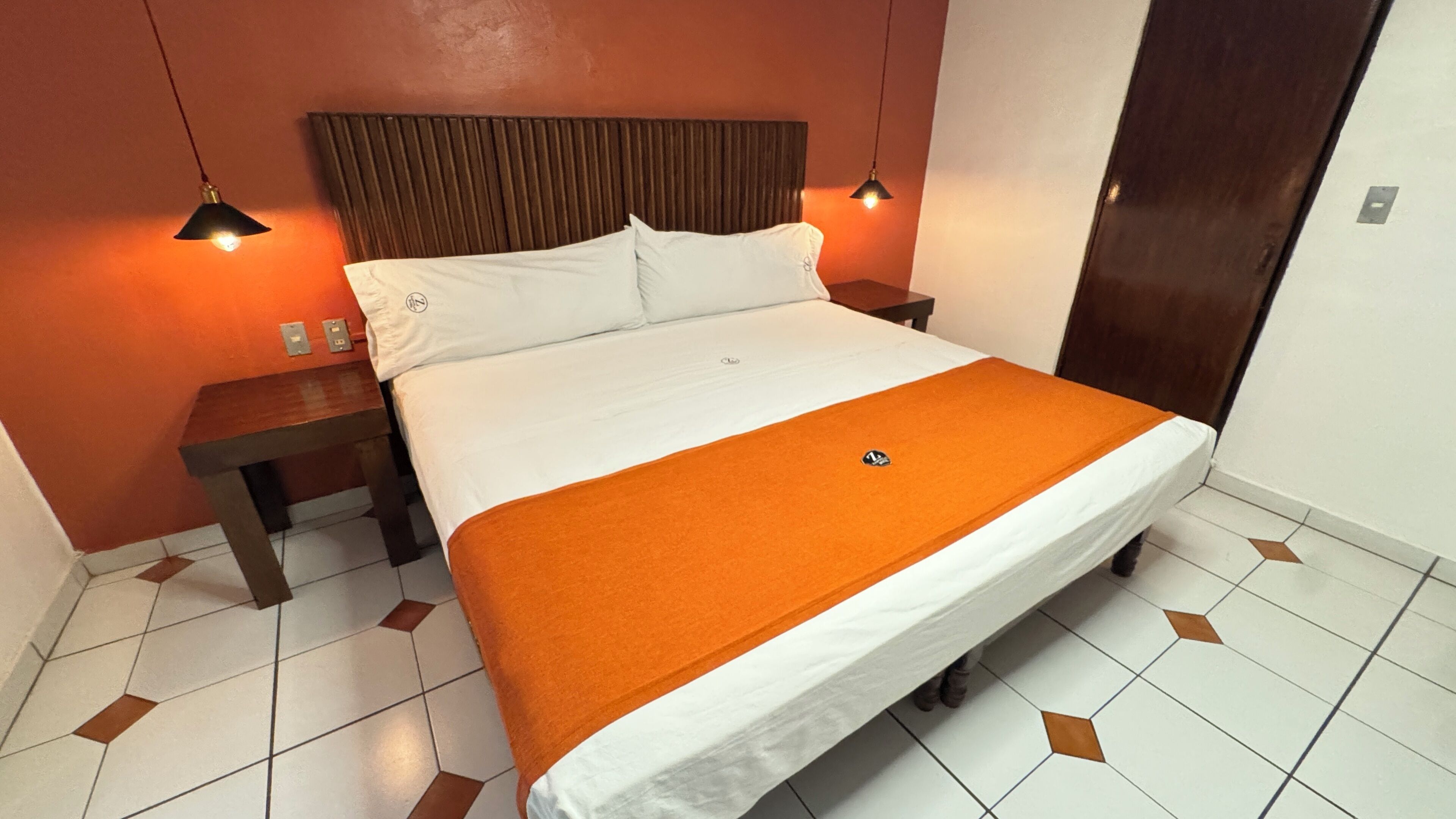 Een hotelkamer met een bed, twee nachtkastjes, een houten hoofdeinde en een deur.