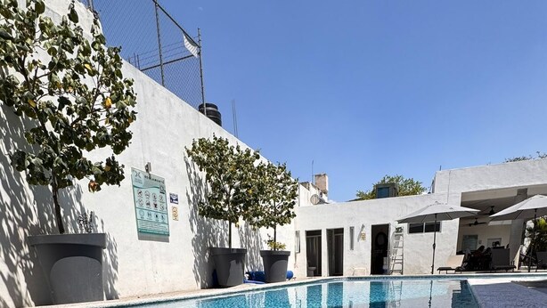 A swimming pool with a tiled edge, surrounded by a building with a white exterior and a fenced area.