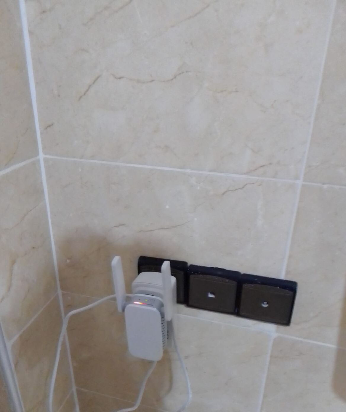 Een betegelde muur met een stopcontact en een verdeeldoos.