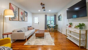 A modern living room with a sofa, coffee table, and a dining area with chairs and a table. - Midtown Cottage - Central Location! 😍 (Duplex) (Tallahassee)