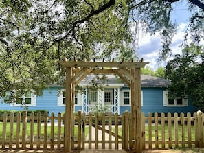A wooden gate leading to a house with a blue exterior and white trim.