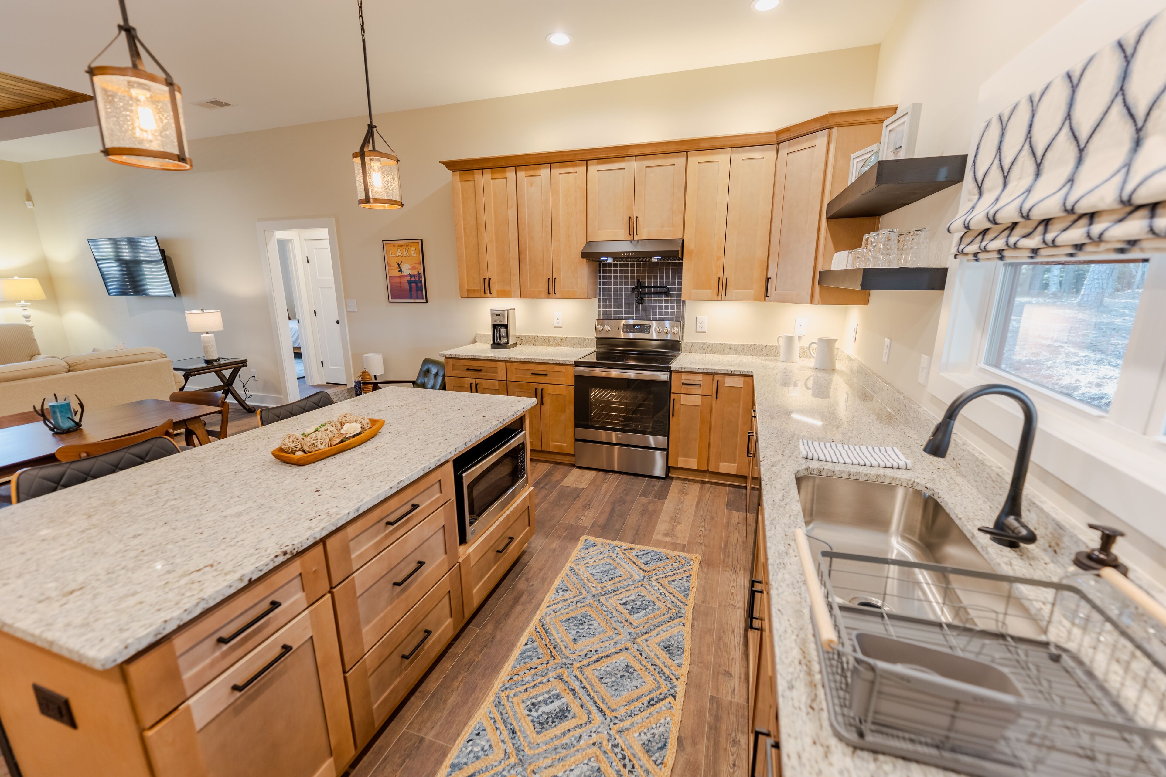 A modern kitchen with wooden cabinets, a large island, stainless steel appliances, and a view of the outdoors.