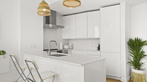 A modern kitchen with white cabinetry, a central island, stainless steel appliances, and wicker pendant lights. - 2 BR Downtown Oasis, AC & stunning views (Vancouver)